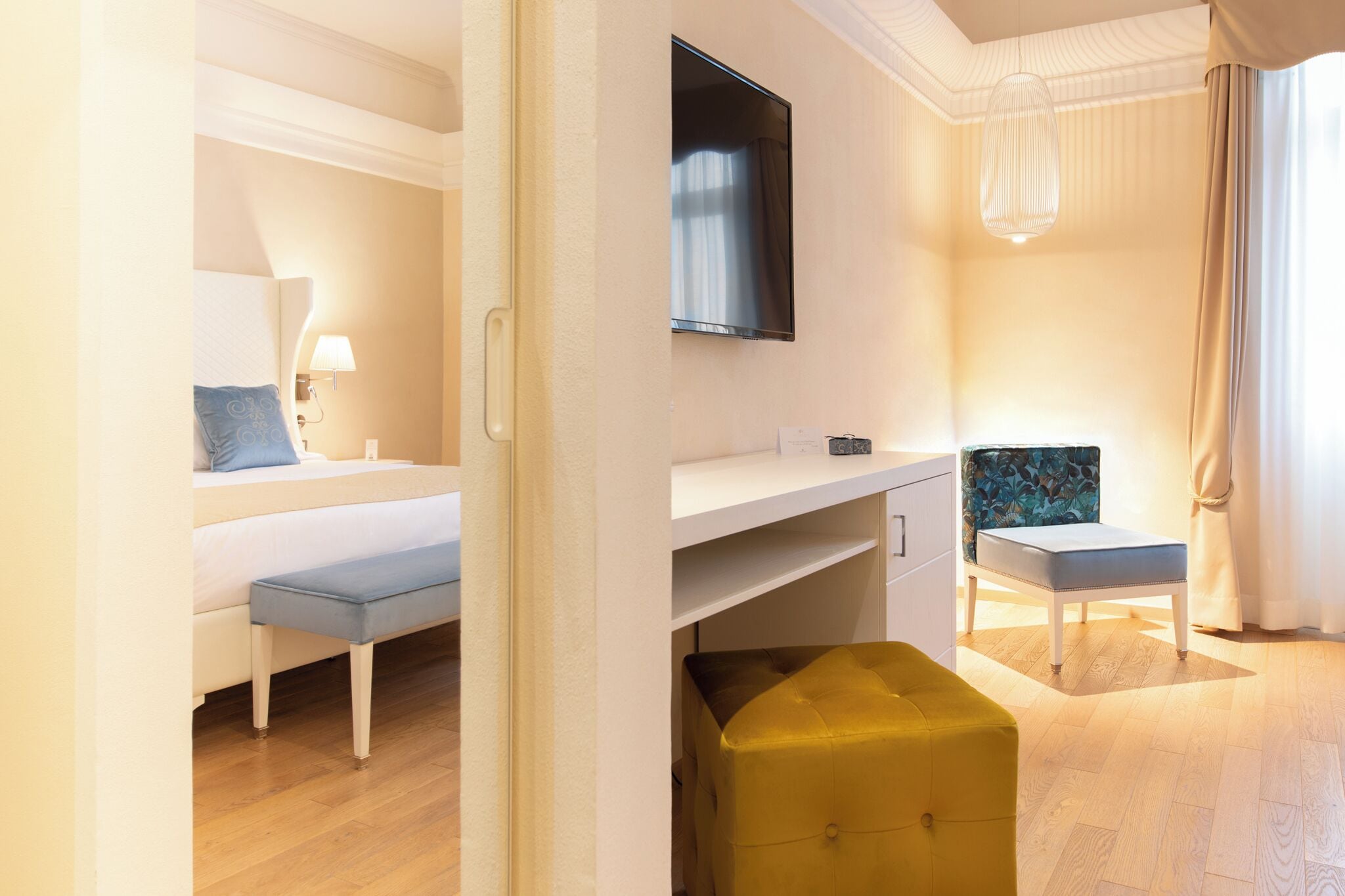 Una habitación de hotel con cama, escritorio, televisor, banco y un pequeño otoman.