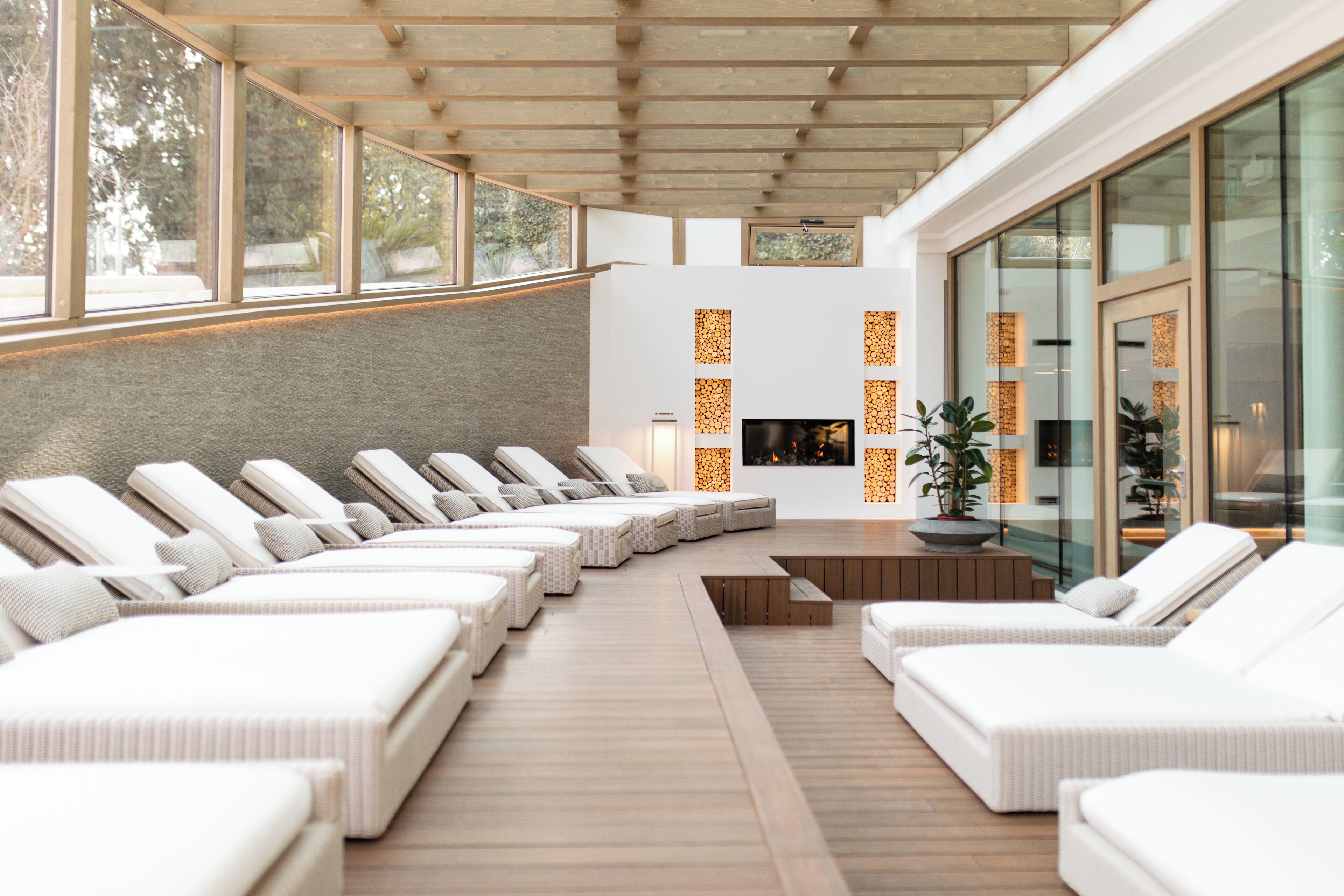 Ein Wellnessbereich mit weißen Liegestühlen, die halbkreisförmig angeordnet sind, Holzboden und einer Steinwand.