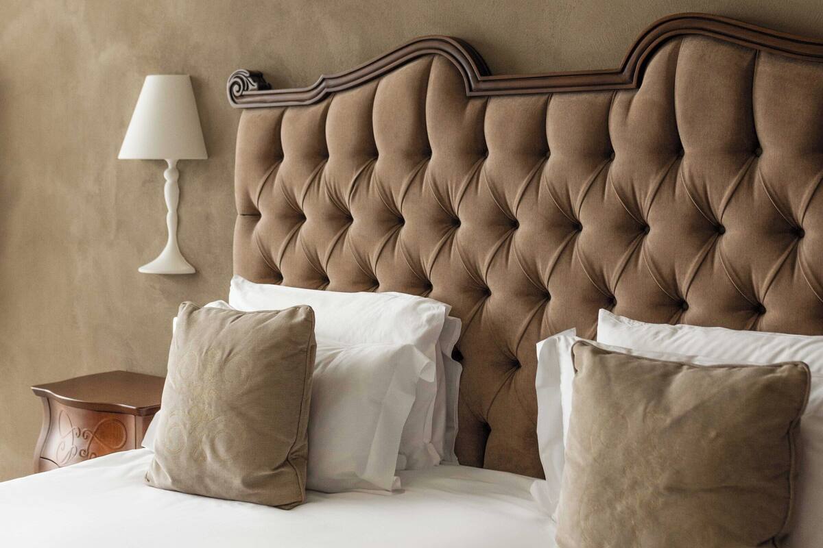 Une chambre à coucher avec une tête de lit capitonnée, du linge de lit blanc et une lampe de chevet.