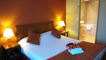 Une chambre d’hôtel avec un grand lit, deux lampes de chevet, une table de chevet et une vue sur une salle de bain équipée d’une baignoire et d’une douche.