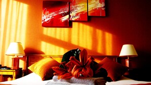 Quarto de hotel com uma cama, duas luminárias de cabeceira, um arranjo floral decorativo e três obras de arte nas paredes.