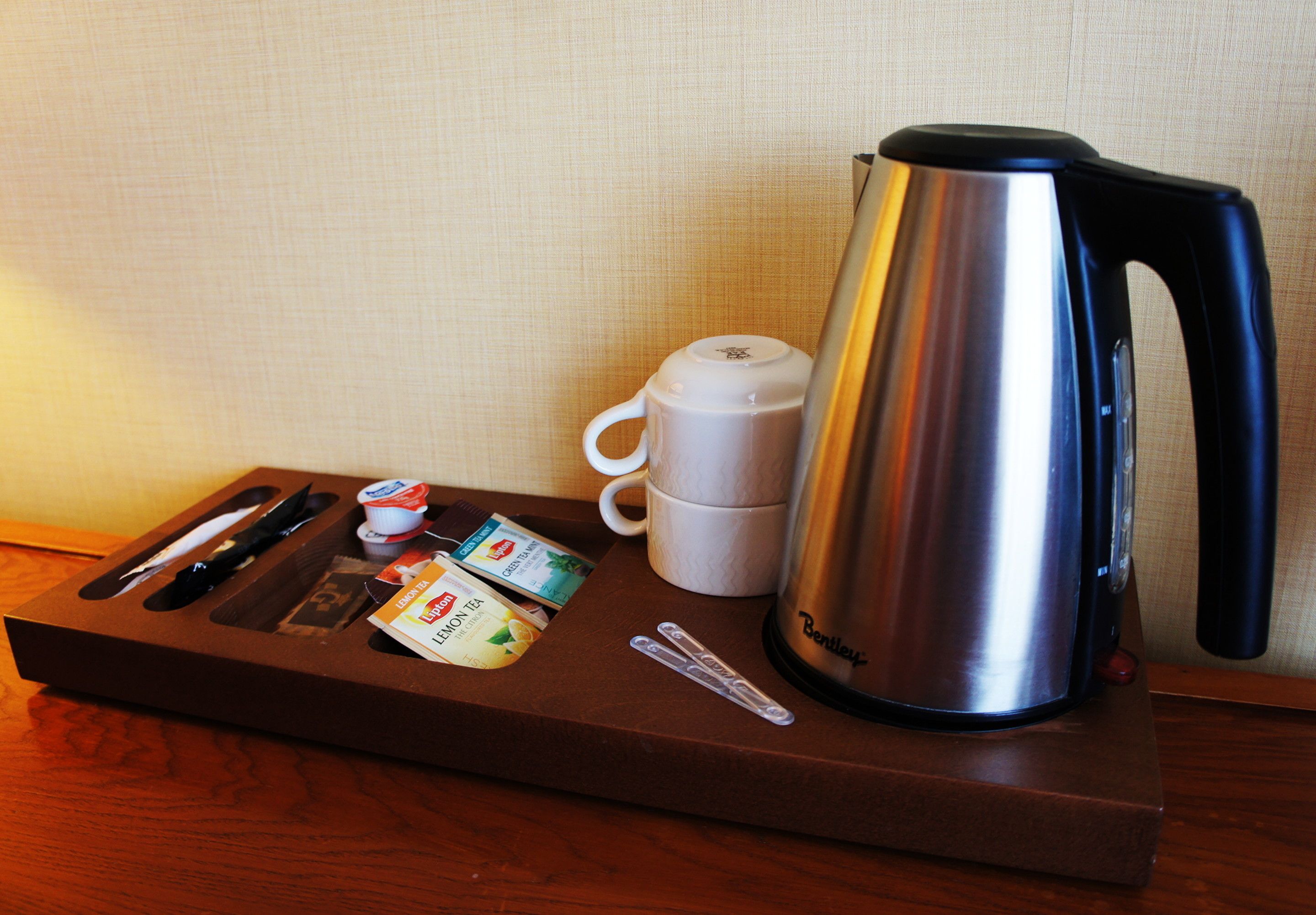A breakfast tray with a stainless steel kettle, white mug, and tea packets.