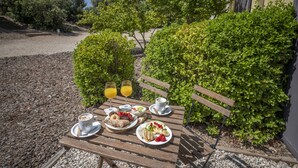Un área de comedor al aire libre con una mesa dispuesta para el desayuno, incluyendo platos de comida, vasos de jugo de naranja y una taza de café.