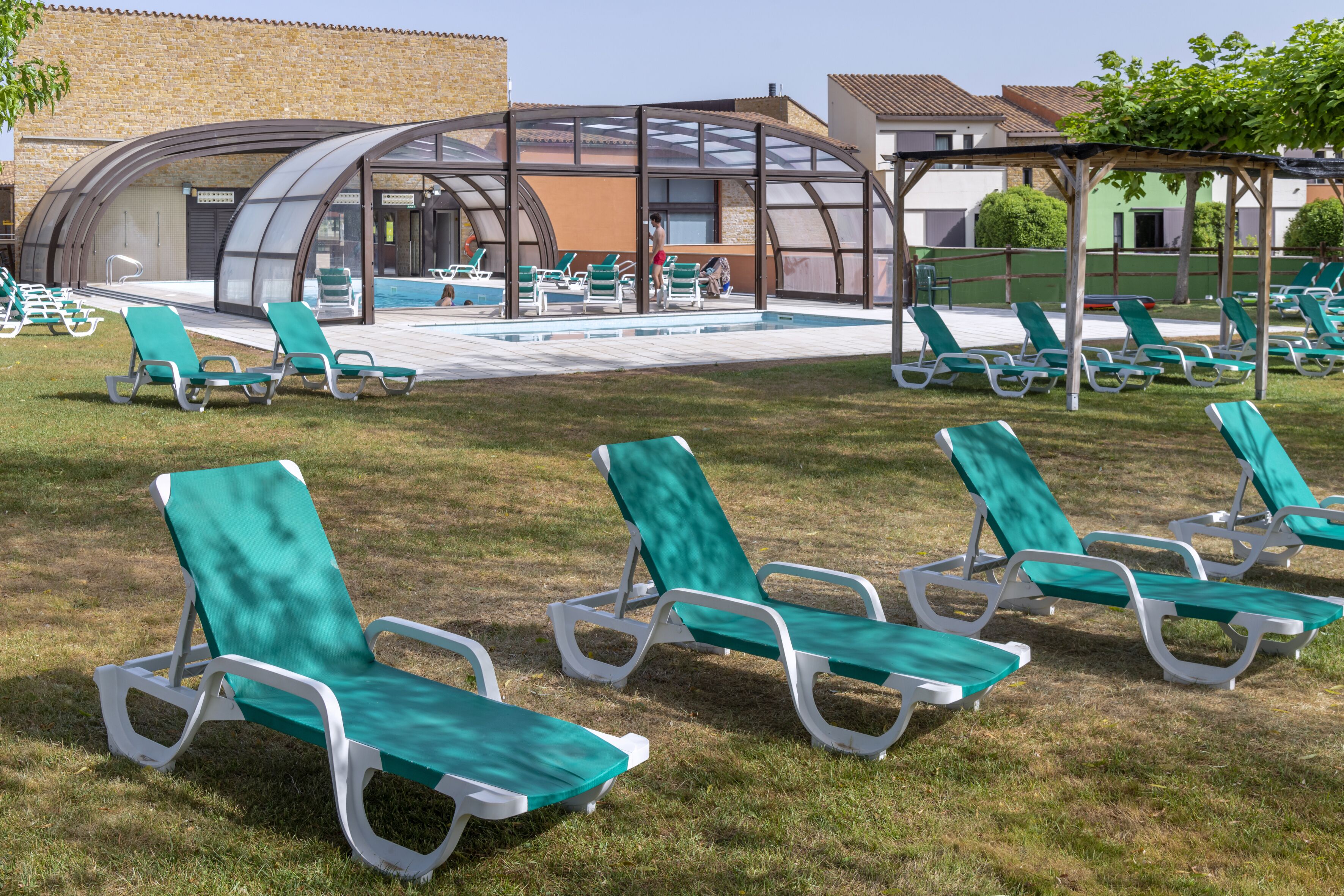 A poolside area with green lounge chairs and a covered seating area.