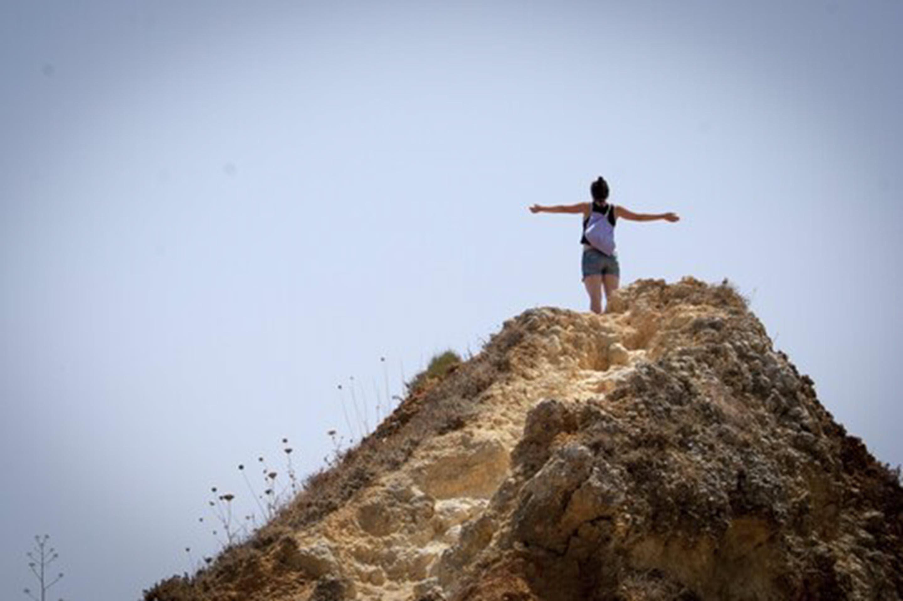 A person standing on a rocky hill with arms outstretched.