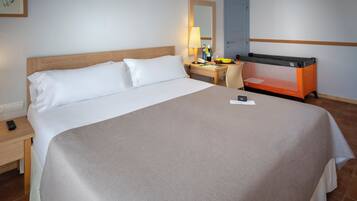 Habitación de hotel con una cama grande, un escritorio con lámpara, una silla y una pequeña mesa con una cesta de frutas.