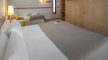 A hotel room with a large bed, a bedside table with a lamp, a small table with fruits, a TV on the wall, and a wardrobe.