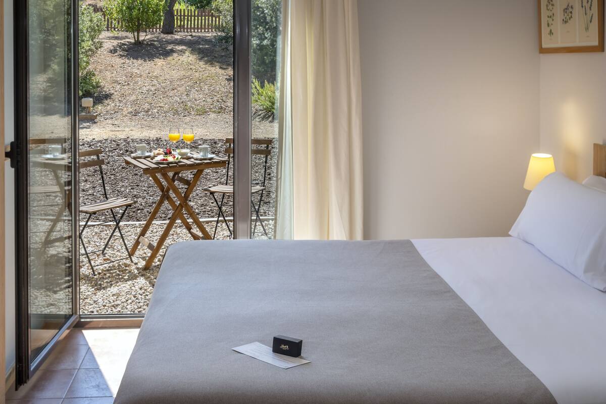 Quarto de hotel com cama, mesa com itens de café da manhã e vista para a área externa.