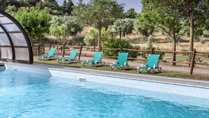 A swimming pool with clear blue water, surrounded by a wooden fence and several green lounge chairs.