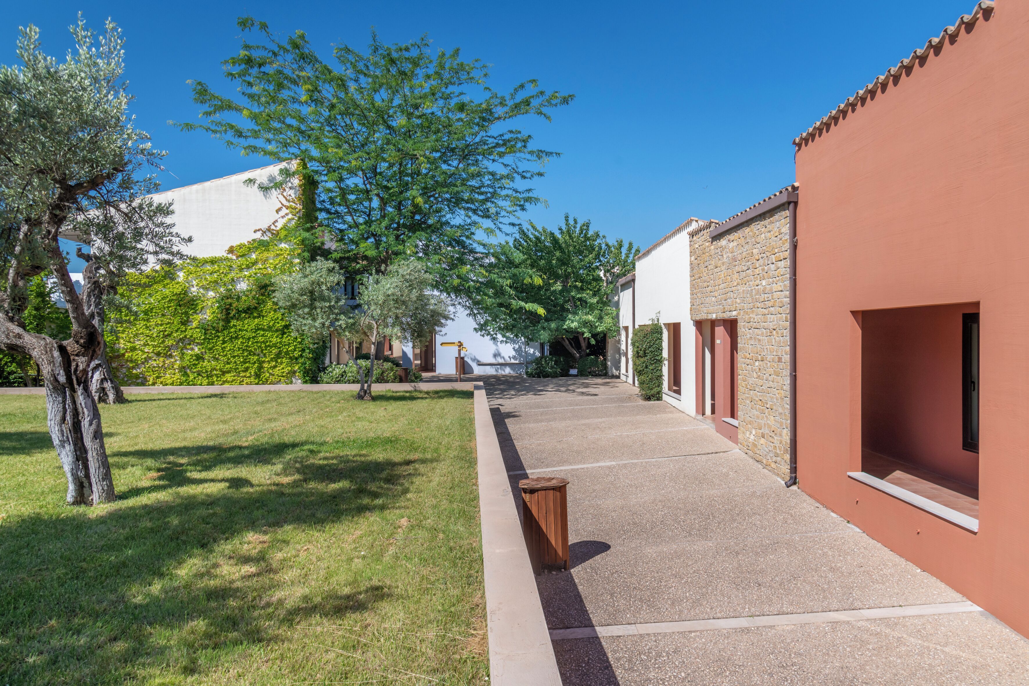 Un patio con un sendero empedrado, un árbol y edificios con fachada roja y muros de piedra.