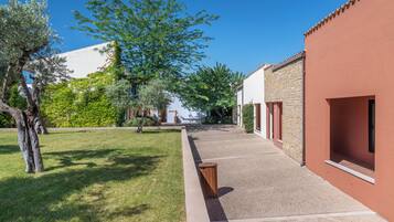 Un patio con un sendero empedrado, un árbol y edificios con fachada roja y muros de piedra.