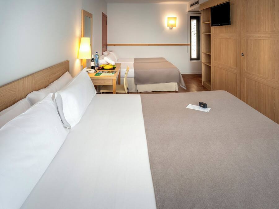 Habitación de hotel con dos camas, un escritorio con lámpara, televisor y armario.