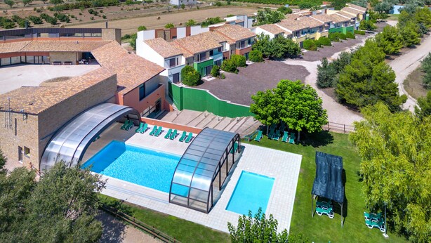 A hotel with a swimming pool, covered outdoor seating, and a view of a vineyard and town in the background.