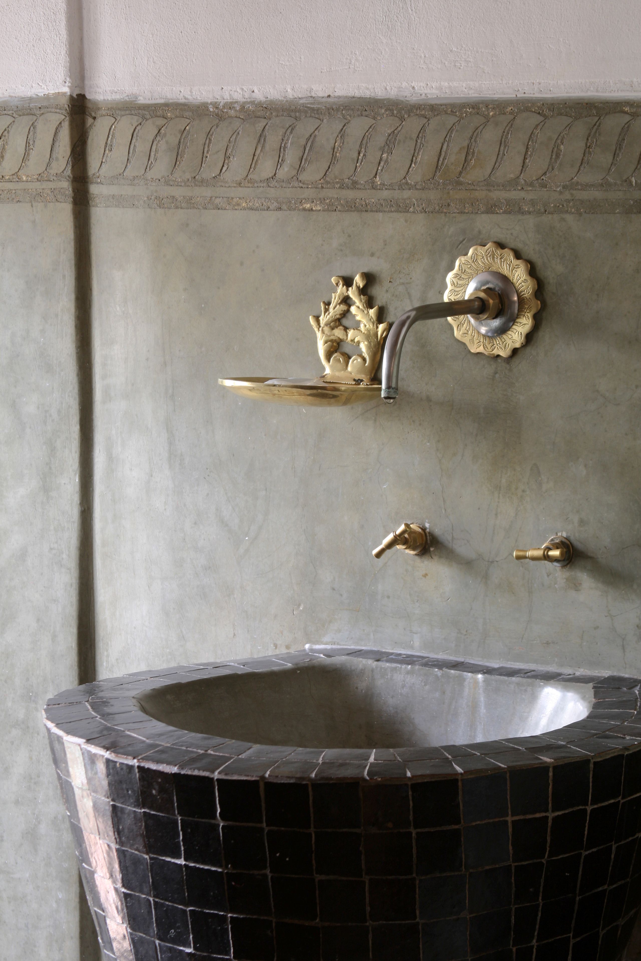 A bathroom with a black mosaic sink, a gold faucet, and a decorative gold crown-shaped handle.
