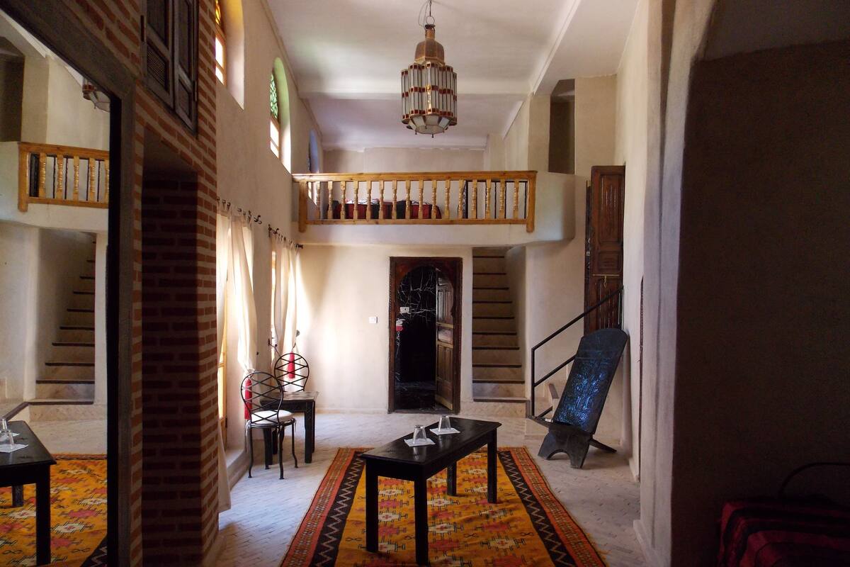 Uma sala de estar ampla com escada, tapete estampado e um candelabro.