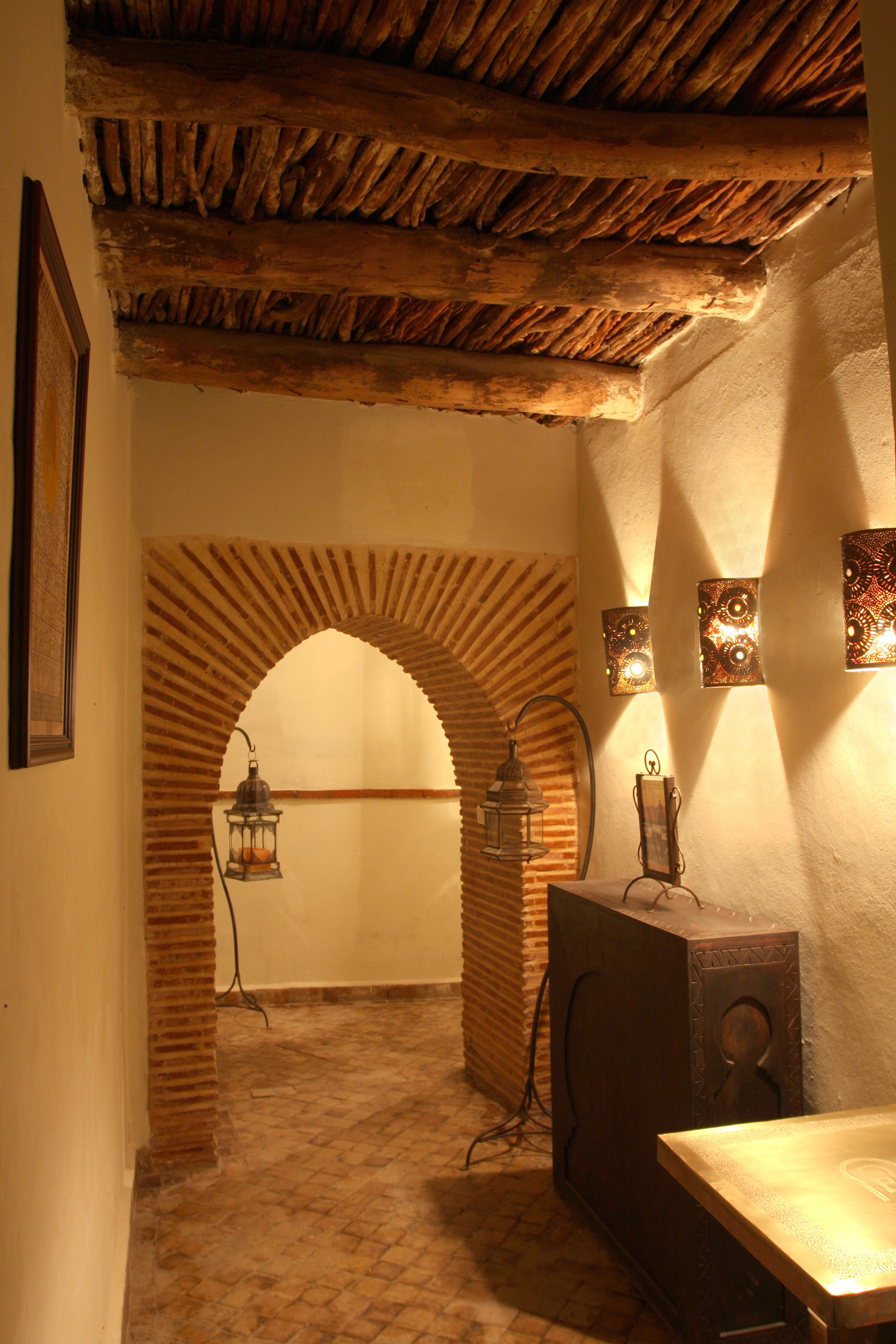A room with a rustic ceiling, a brick archway, a wooden table, and wall-mounted lights.