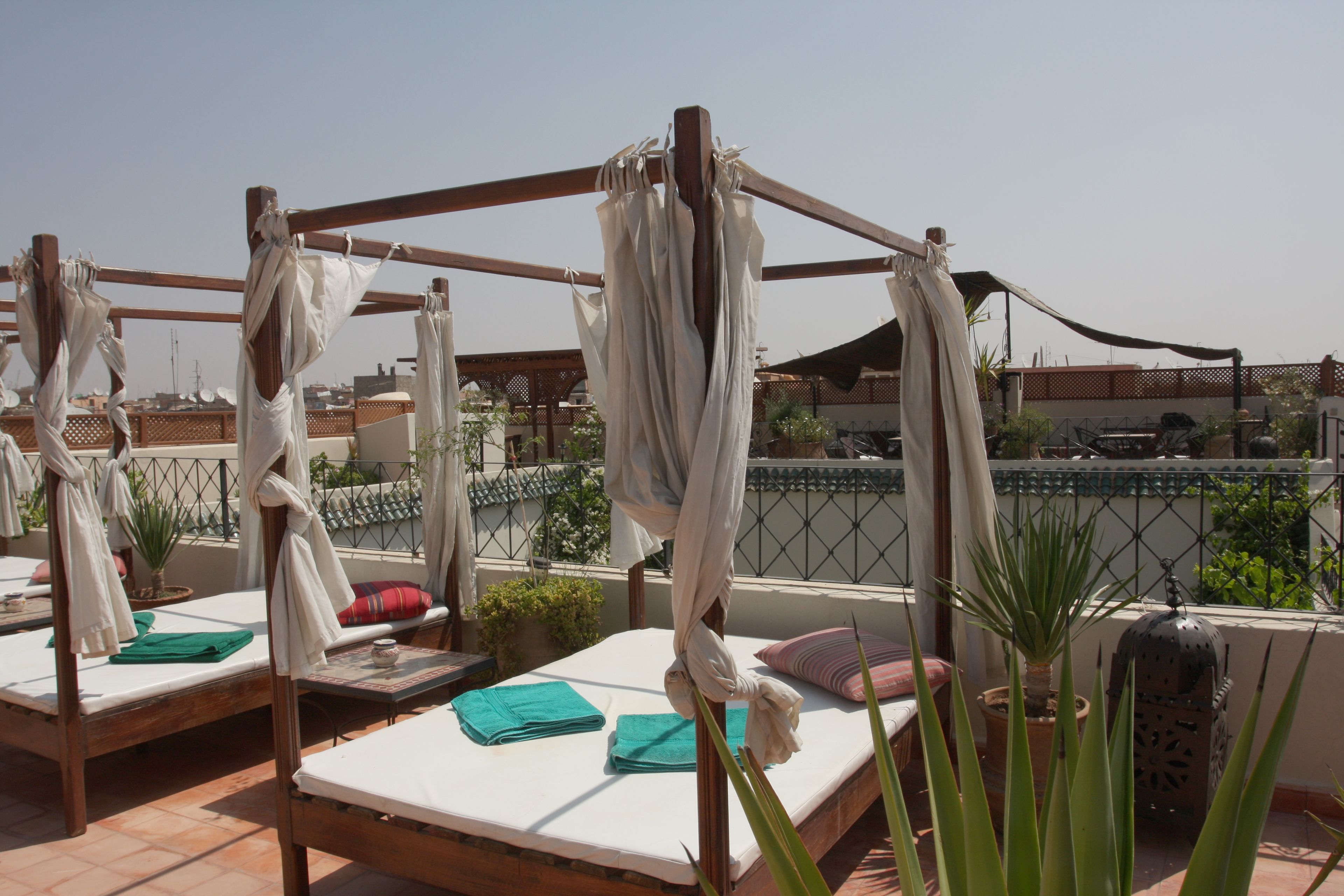 A rooftop terrace with wooden beds, green towels, and potted plants.