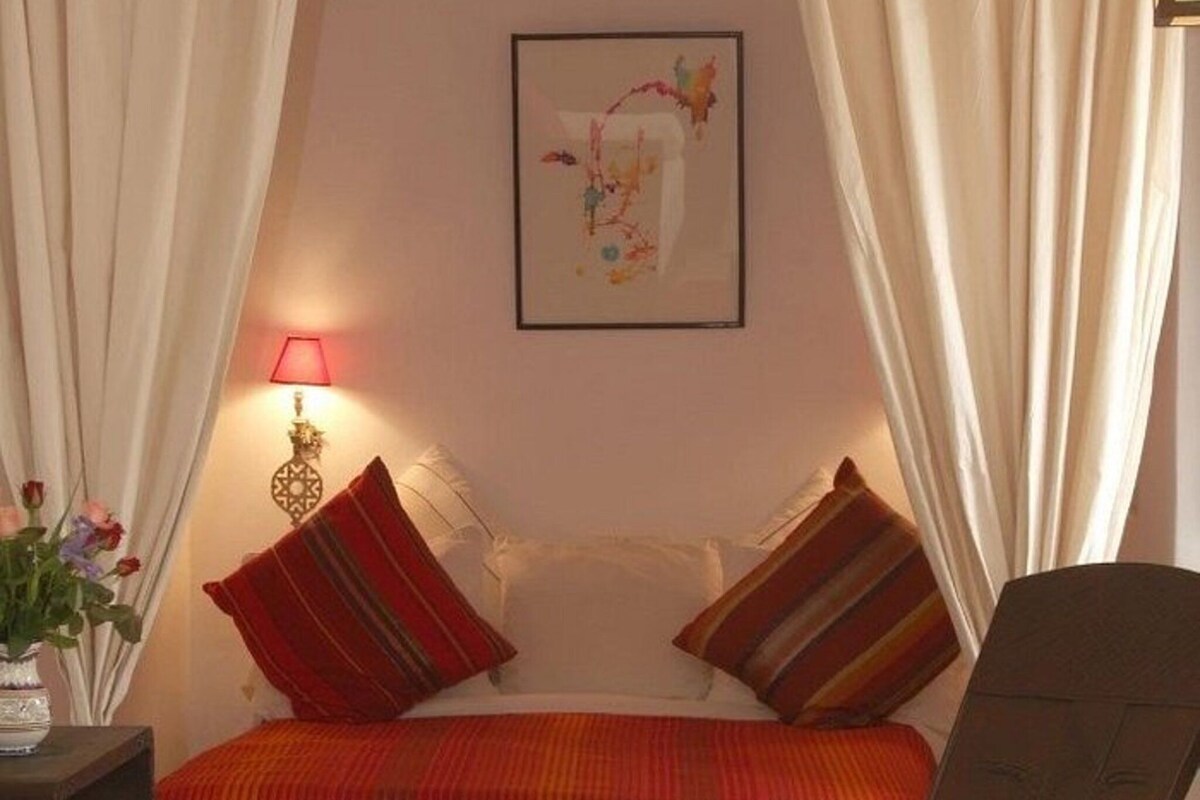 Une chambre à coucher avec un lit, des oreillers, une table de chevet, une lampe et un tableau au mur.