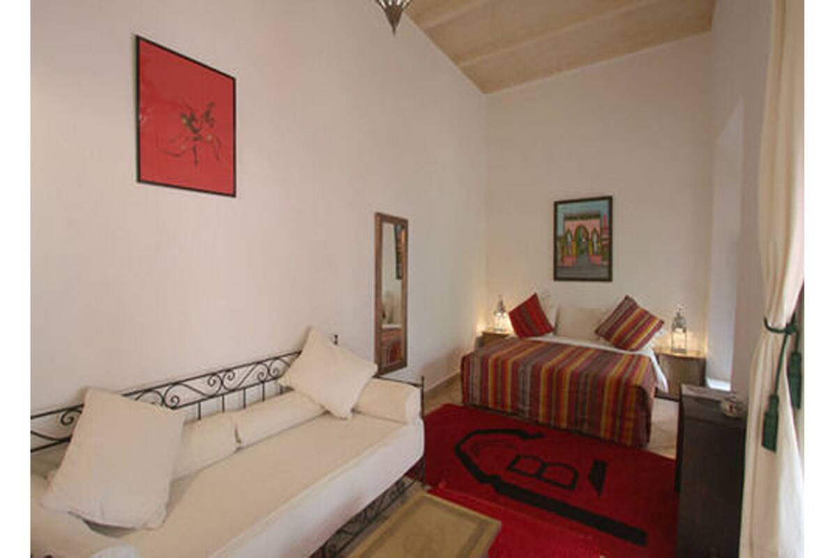 Um quarto com cama, sofá, espelho e duas pinturas nas paredes.