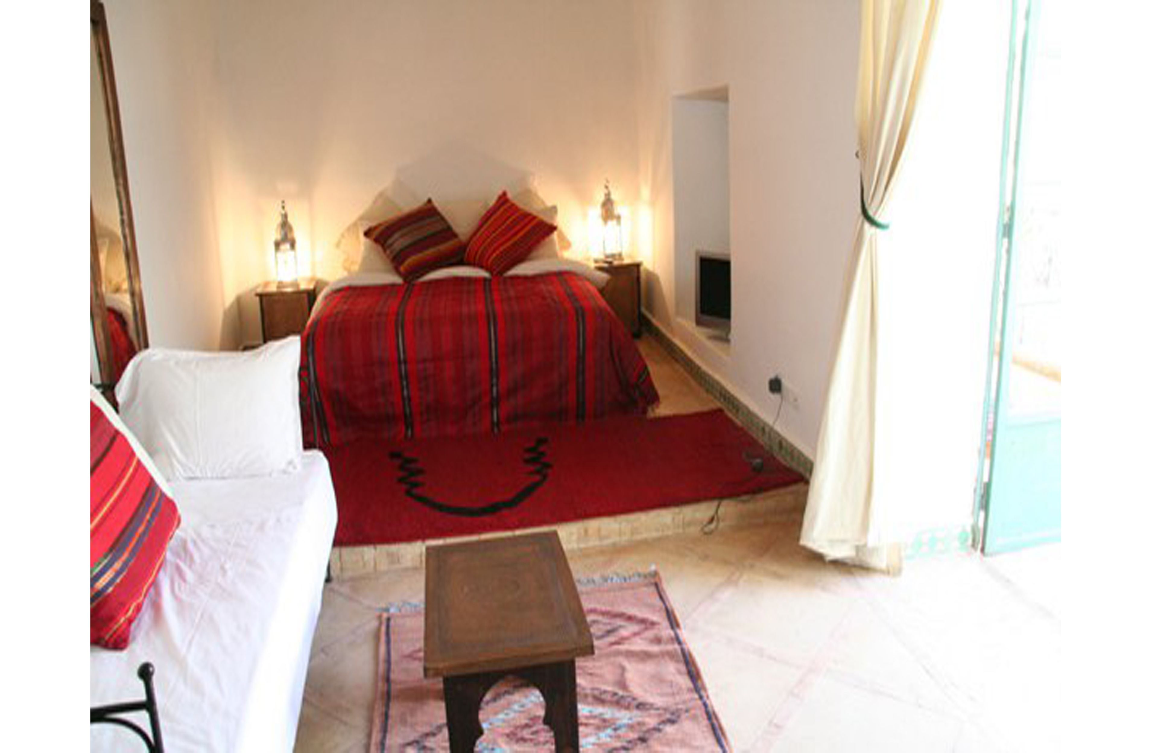 A bedroom with a bed, a chair, a small table, and a window with curtains.