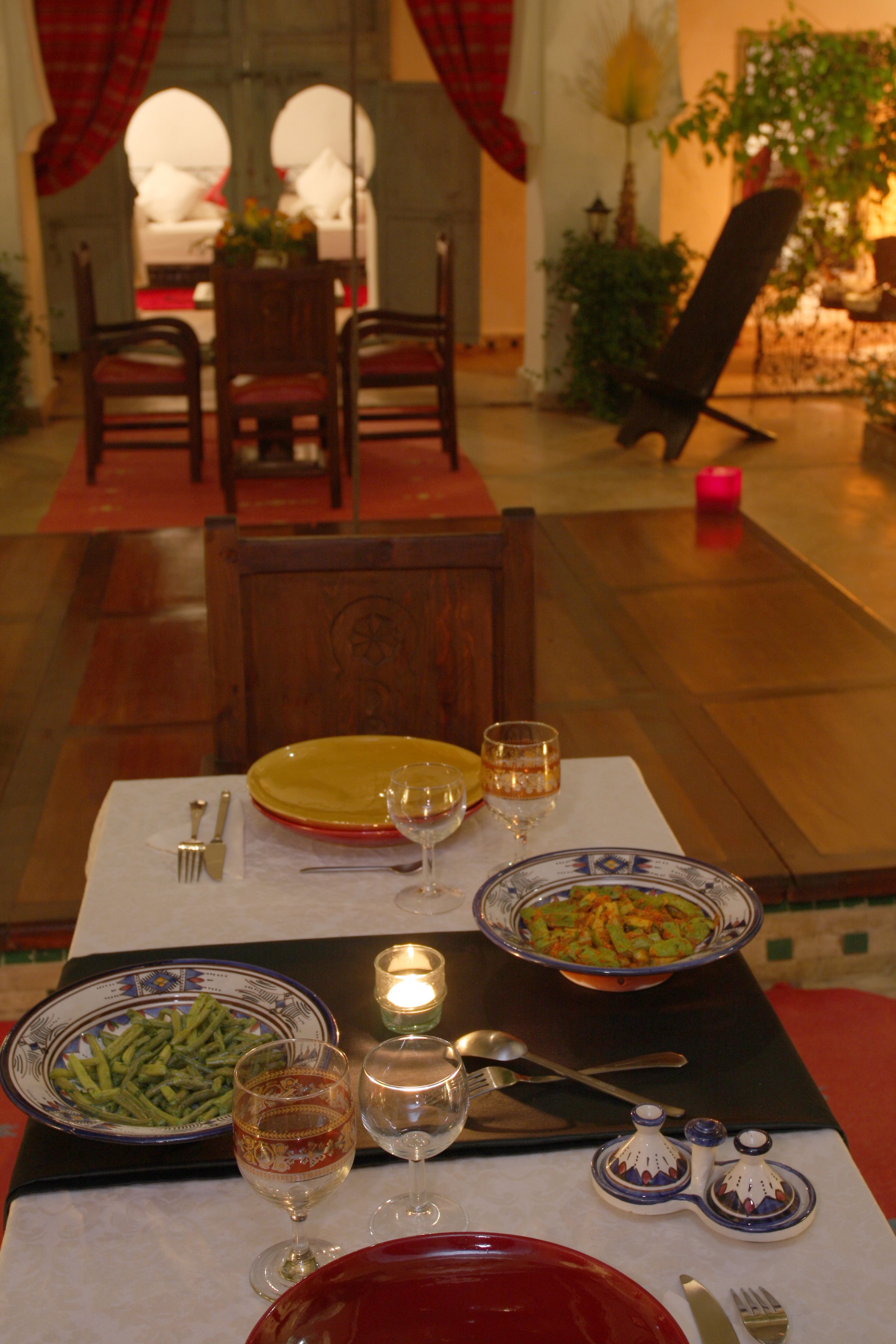 Une table à manger dressée avec des assiettes, des couverts et des verres, avec une bougie et une plante en arrière-plan.