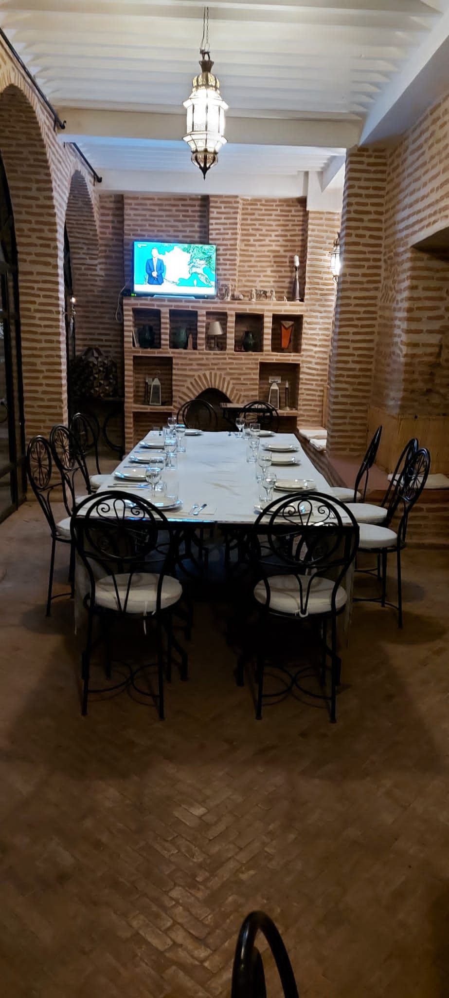 A dining area with a brick wall, a chandelier, and a television mounted on the wall.