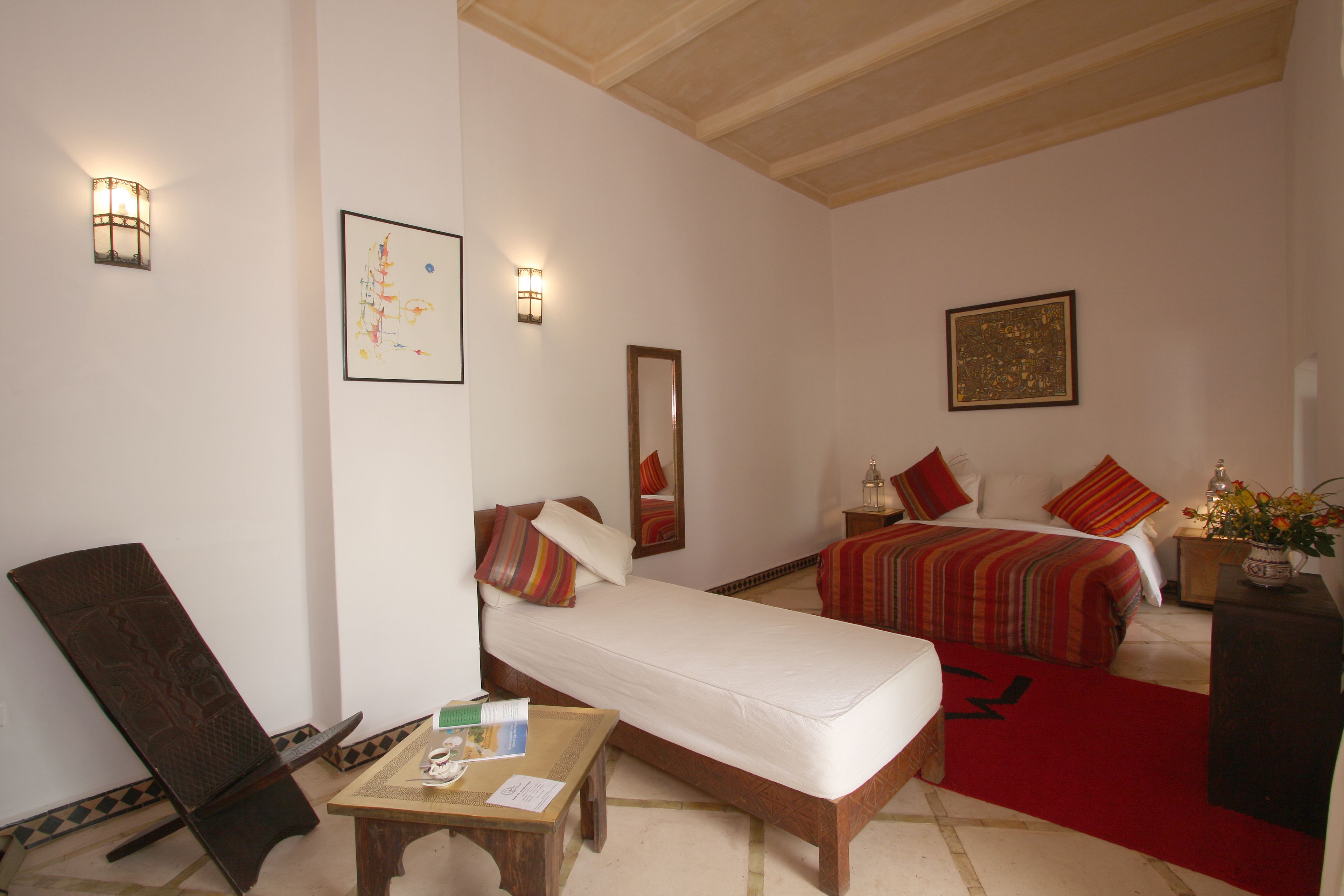 A hotel room with a single bed, a chair, a small table, and a nightstand with a vase of flowers.
