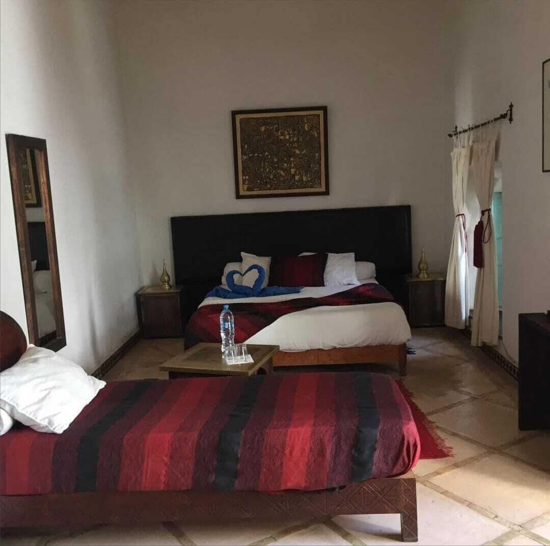 A hotel room with two beds, a nightstand, a bedside table, a mirror, and a painting on the wall.