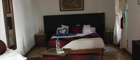 A hotel room with two beds, a nightstand, a bedside table, a mirror, and a painting on the wall.