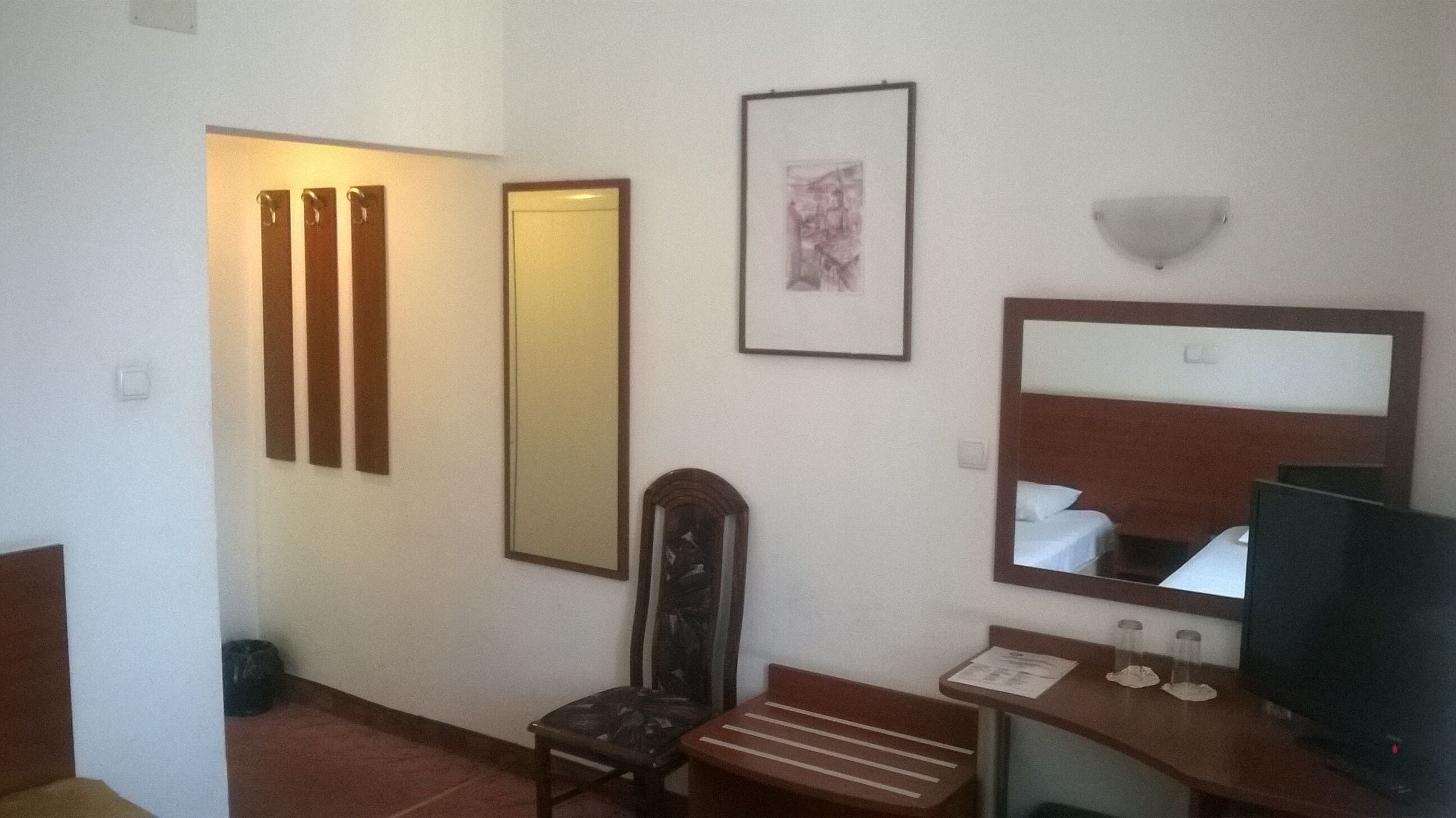 Ein Hotelzimmer mit einem Bett, einem Schreibtisch mit Computer, einem Sessel, einem Spiegel und einem gerahmten Bild an der Wand.