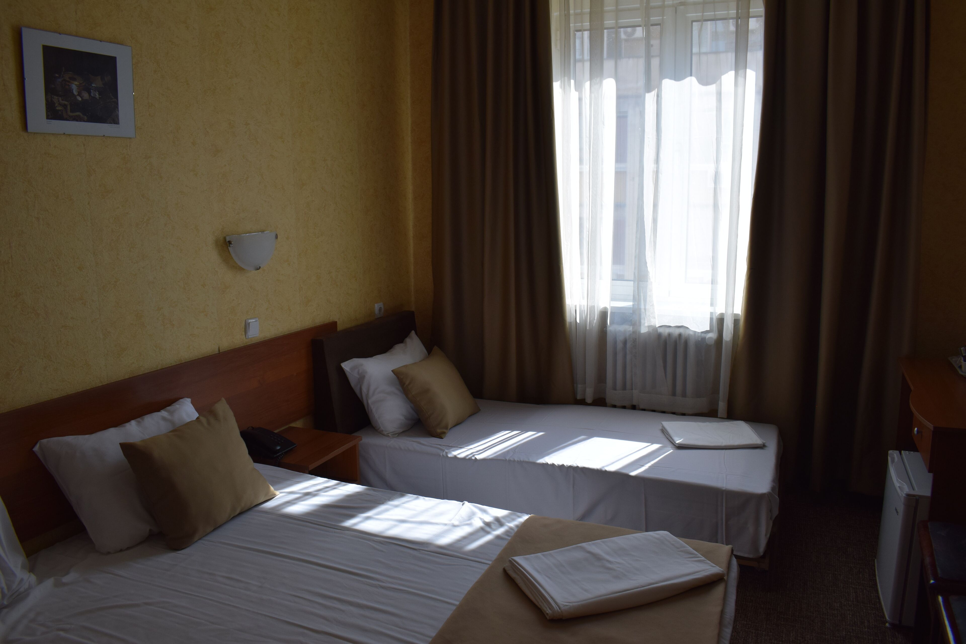 A hotel room with two beds, a nightstand, a desk, and a window with curtains.