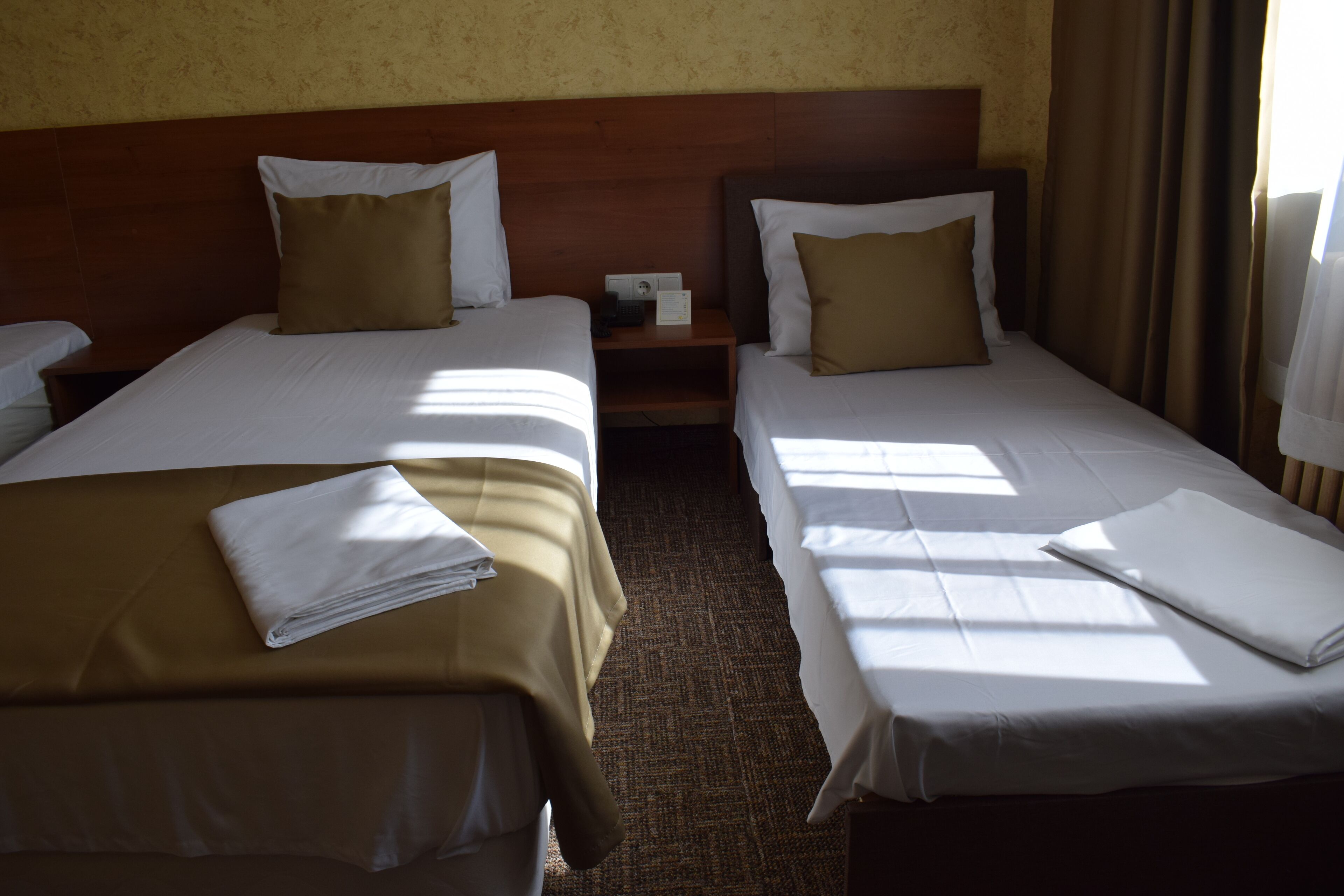 A hotel room with two single beds, each with a brown pillow and white sheets.