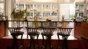 En restaurant med udsigt til en bygning med flere etager og balkoner. Flere krukkeplanter og et par stole rundt om et bord.