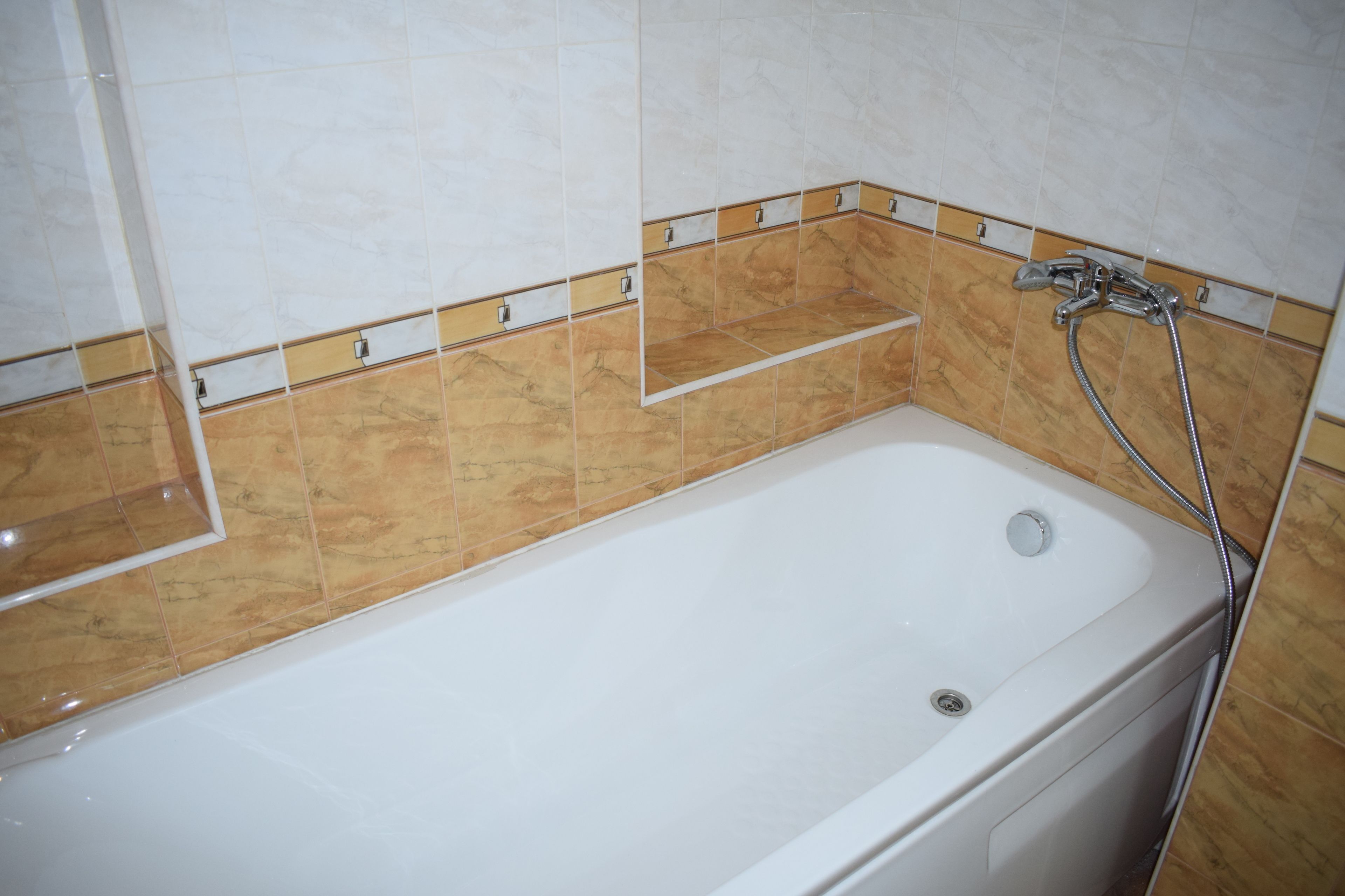 A bathroom with a white bathtub, a shower area, and a tiled wall with a beige and white pattern.