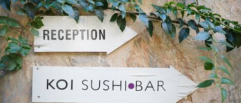 Dos señales direccionales en una pared, una con la etiqueta 'RECEPTION' y la otra con la etiqueta 'KOI SUSHI BAR'.