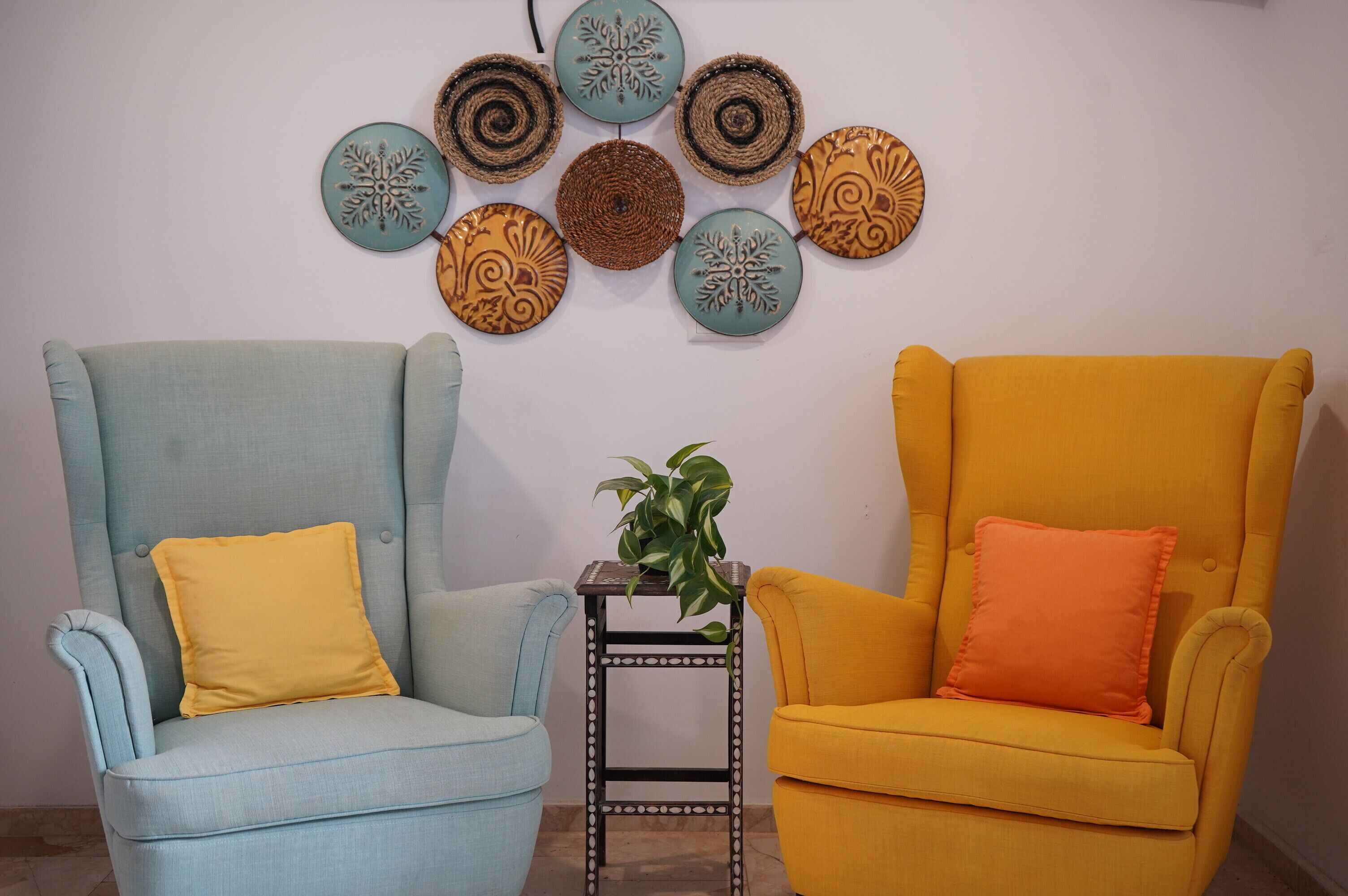 Deux fauteuils avec des coussins jaunes, une petite table avec une plante et des assiettes décoratives accrochées au mur.