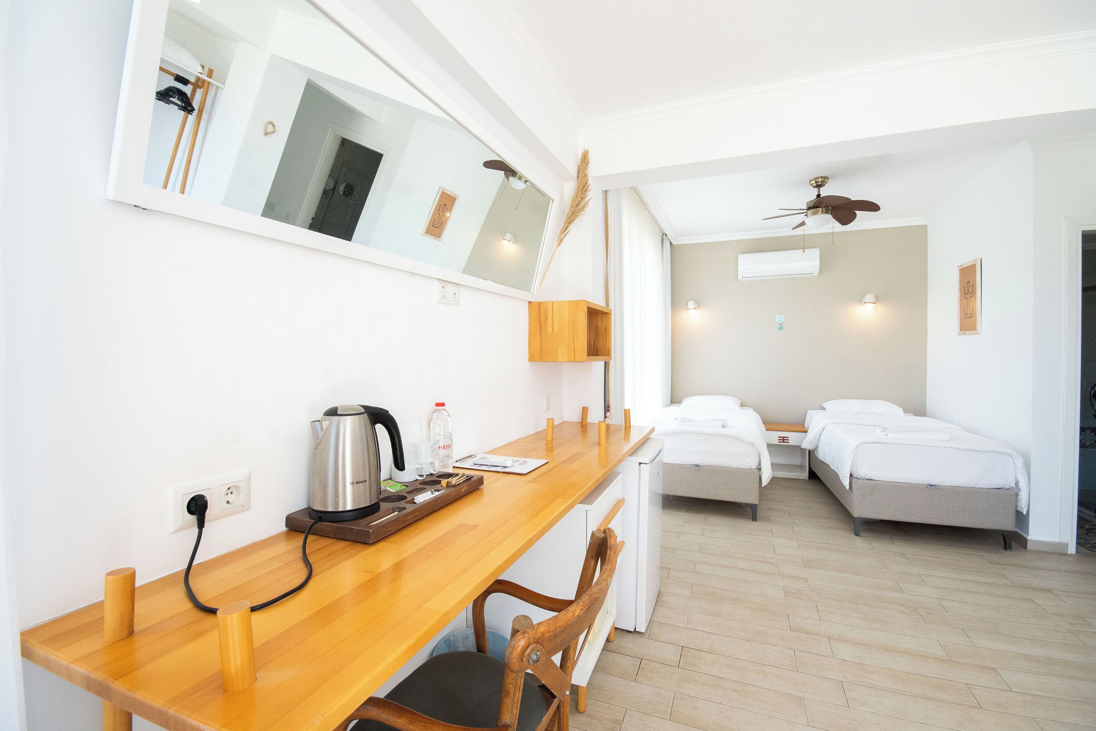 A compact room with a wooden desk, a bed, a ceiling fan, and a mirror.
