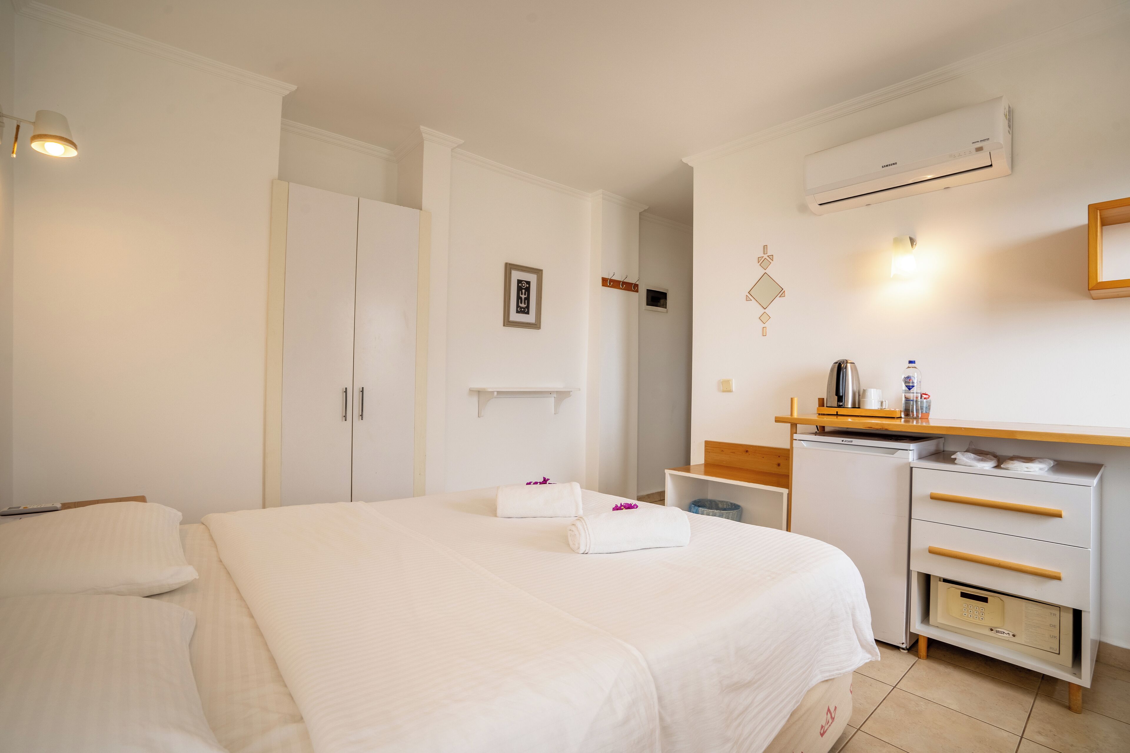 Habitación de hotel con una cama grande, un escritorio con silla, una kitchenette pequeña y un equipo de aire acondicionado.
