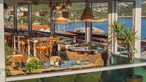 Restaurante con vistas a un puerto deportivo y barcos, con mobiliario de mimbre y lámparas colgantes.