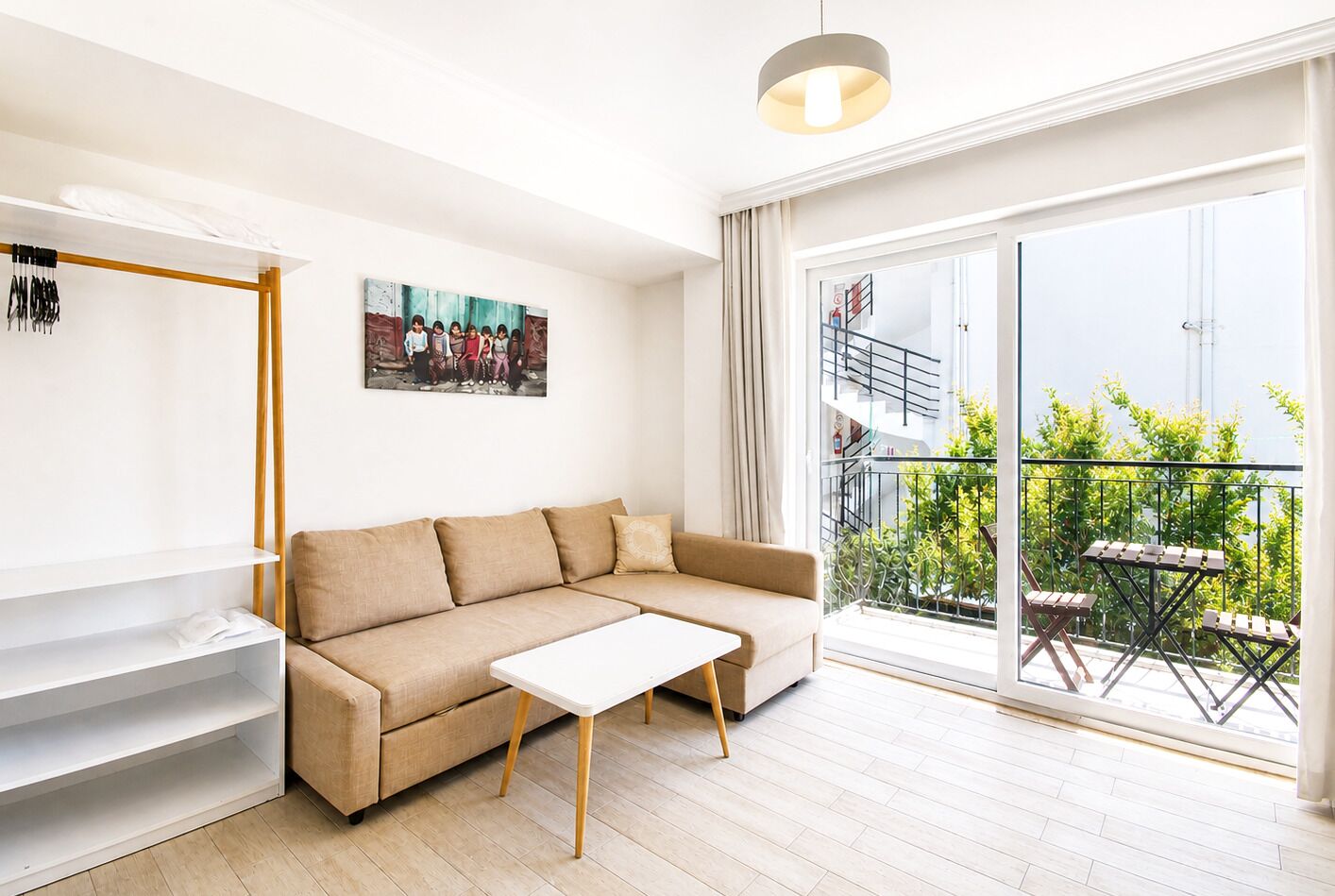 Ein modernes Wohnzimmer mit einem beigen Sofa, einem weißen Couchtisch und einem großen Fenster mit Blick auf einen Balkon.