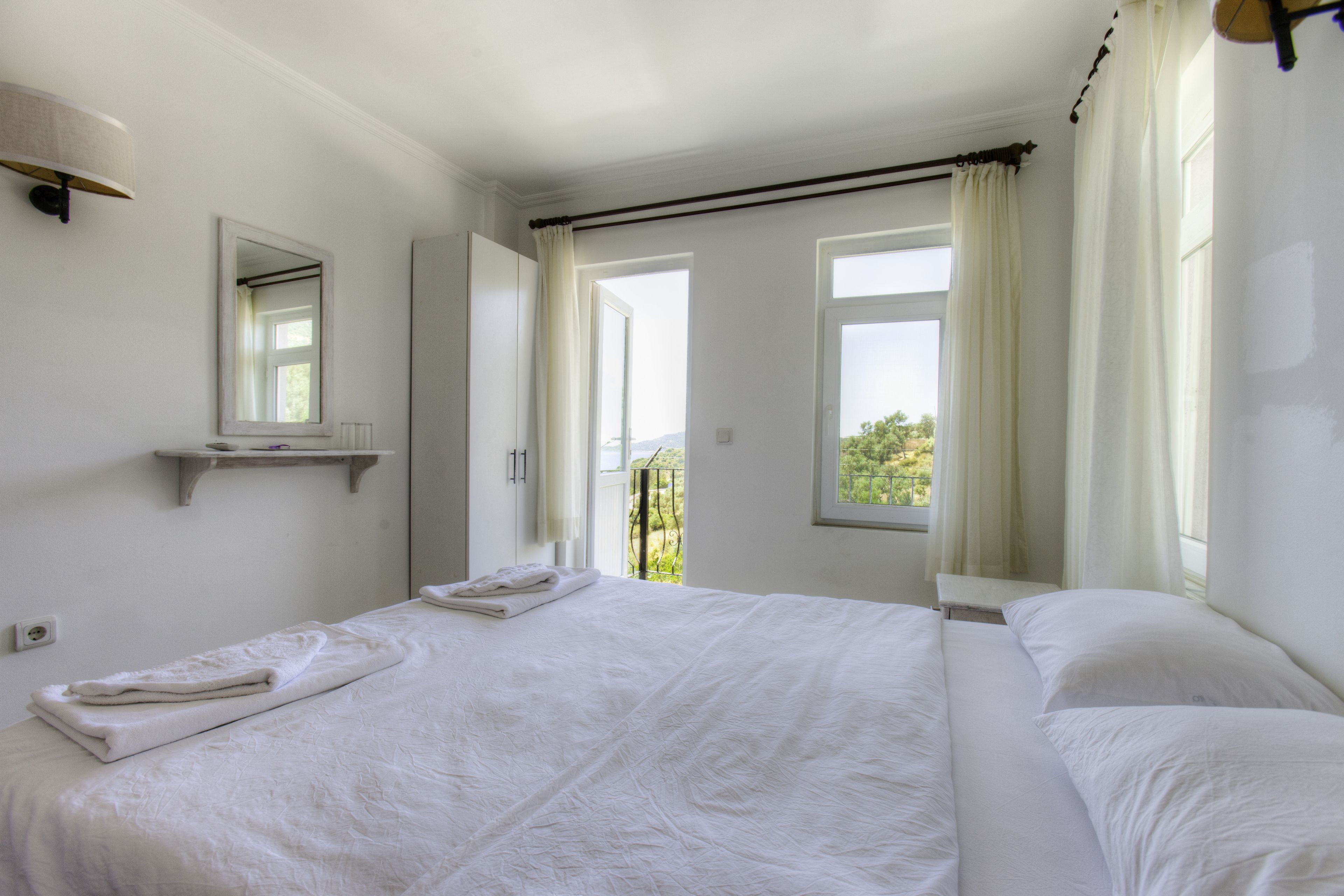 A hotel room with a large bed, a bedside table, a mirror, and a window with curtains.