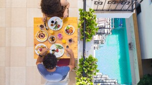 Comedor con vistas a la piscina, con una mesa de madera, platos de comida, sillas blancas y plantas en macetas.