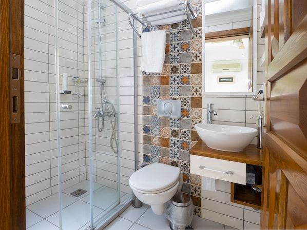 A bathroom with a glass-enclosed shower, a white toilet, and a sink with a wooden countertop. - Hideaway Hotel (Kas)