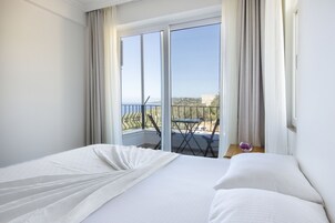 A hotel room with a large bed, a balcony with a table and chairs, and a view of the sea.