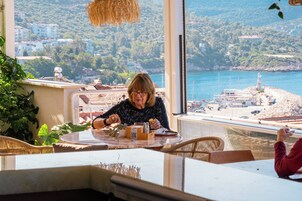 Una mujer cenando en una mesa con vistas a un pueblo costero y un faro.