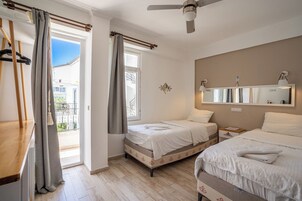 Ένα δωμάτιο ξενοδοχείου με δύο κρεβάτια, έναν ανεμιστήρα οροφής, έναν μεγάλο καθρέφτη και ένα μπαλκόνι με κουρτίνες.