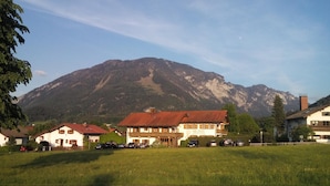 Um hotel com telhado vermelho, cercado por um campo gramado e uma montanha ao fundo.