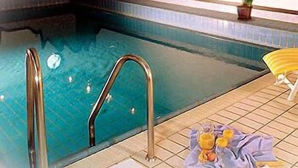 Uma piscina com uma escada de metal, um vaso de planta e uma toalha no chão.