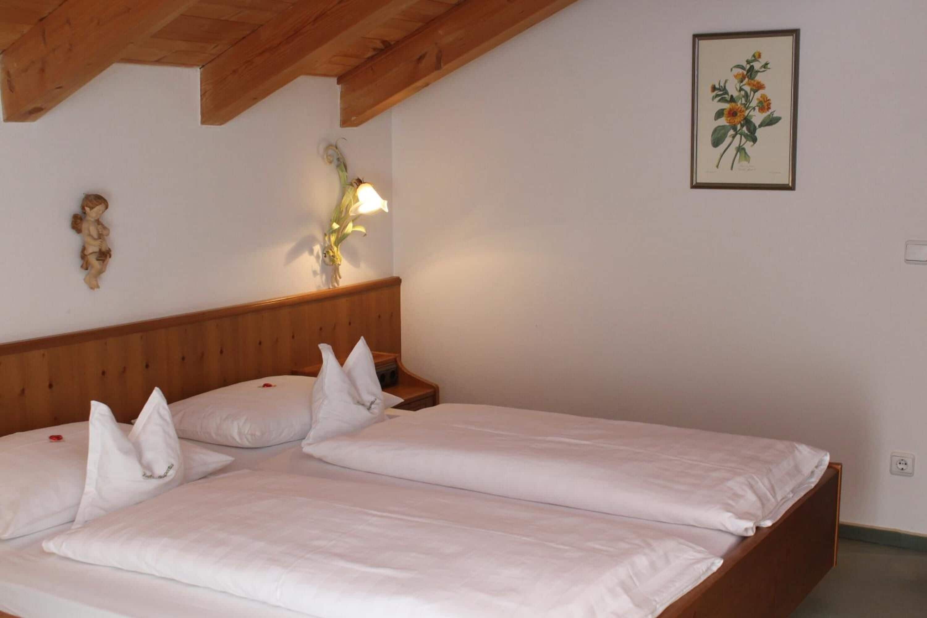 Een slaapkamer met twee bedden, een houten hoofdbord, nachtlampjes en een ingelijste botanische afbeelding aan de muur.