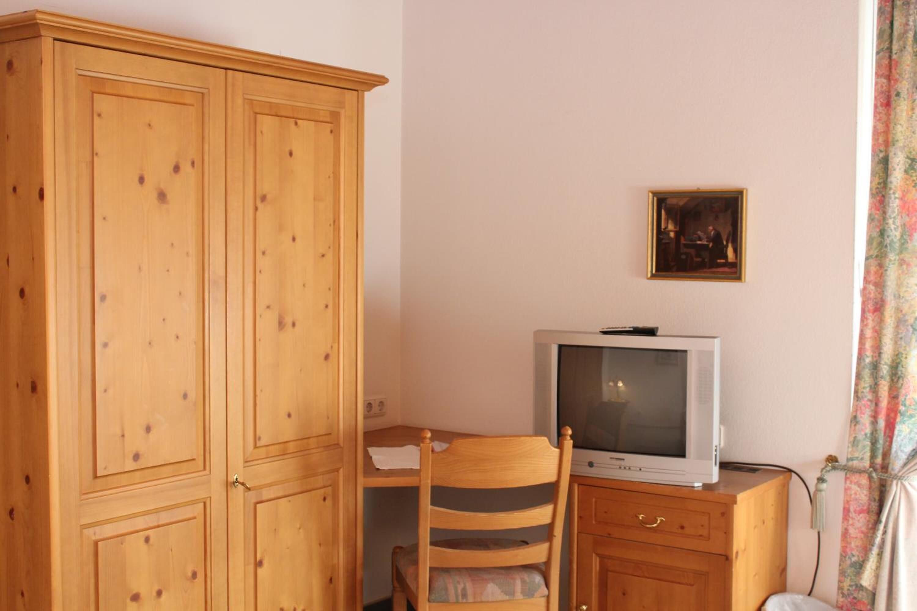Ein Zimmer mit einem Holzschrank, einem Holztisch mit Fernseher und einem Stuhl.